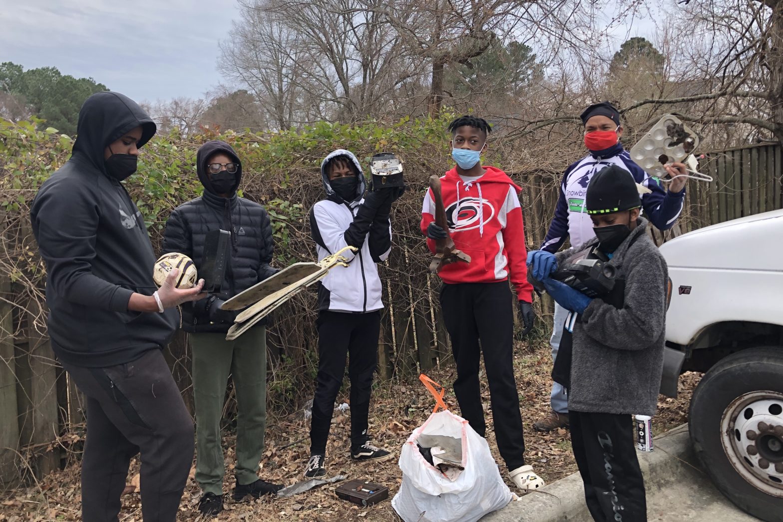 Four Triangle Bikeworks youth and one coach standing in parking lot of CommunityWorx holding objects found while on MLK Day of Service